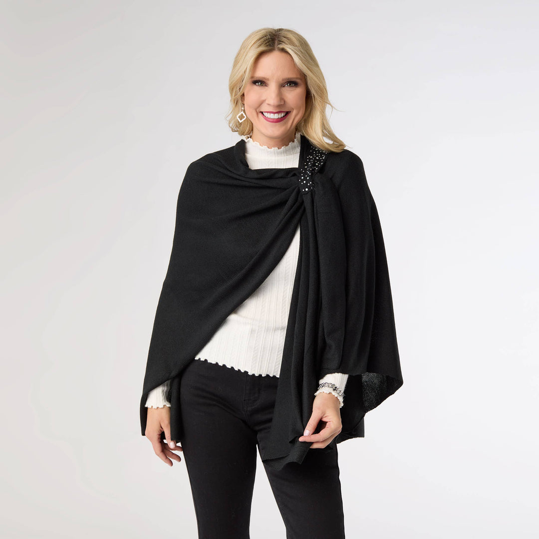 Woman wearing a black shawl over a white top and black pants on a light gray background