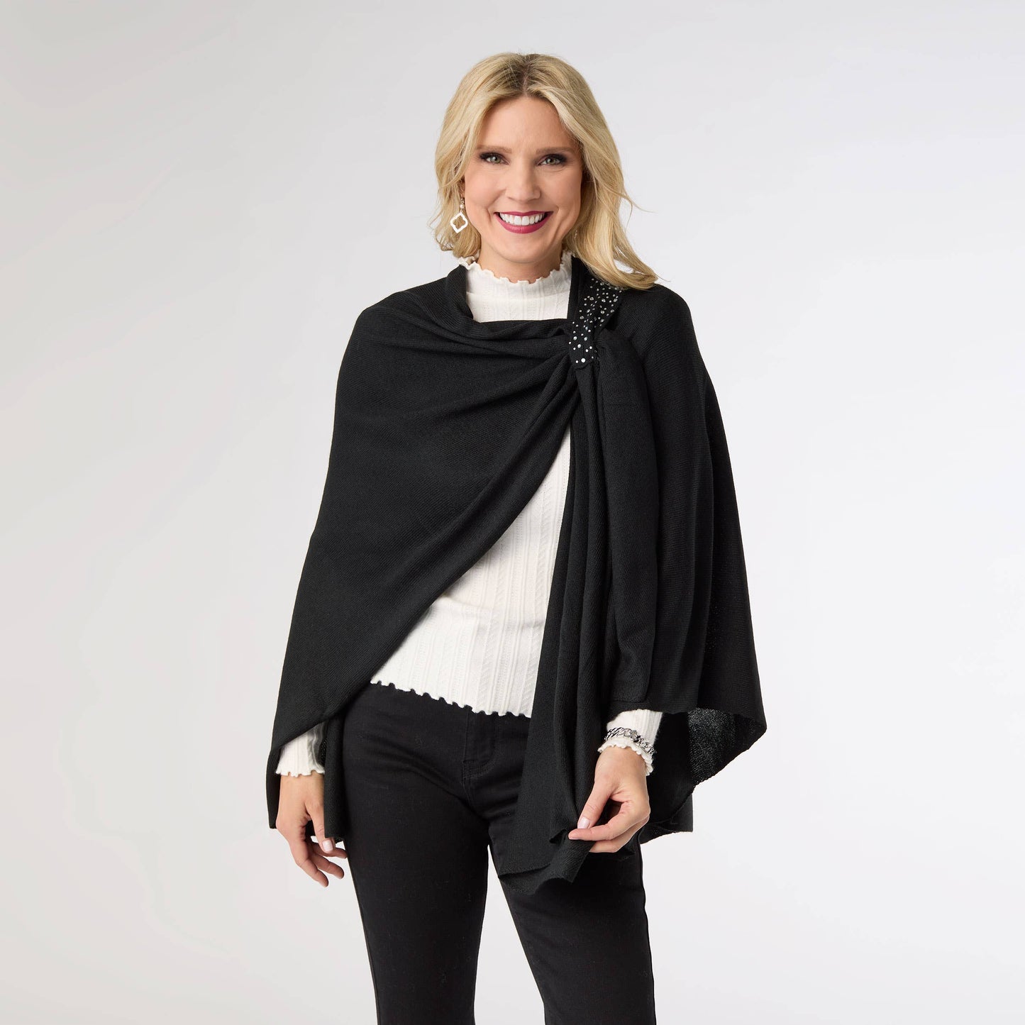 Woman wearing a black shawl over a white top and black pants on a light gray background