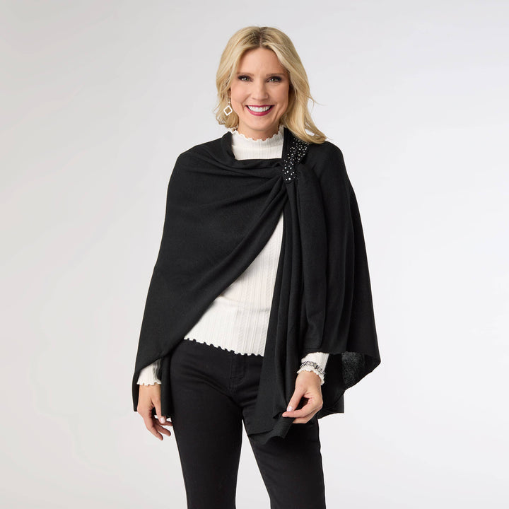Woman wearing a black shawl over a white top and black pants on a light gray background