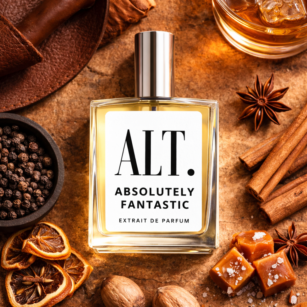 Perfume bottle labeled 'ALT. Absolutely Fantastic' surrounded by spices and caramel on a wooden surface