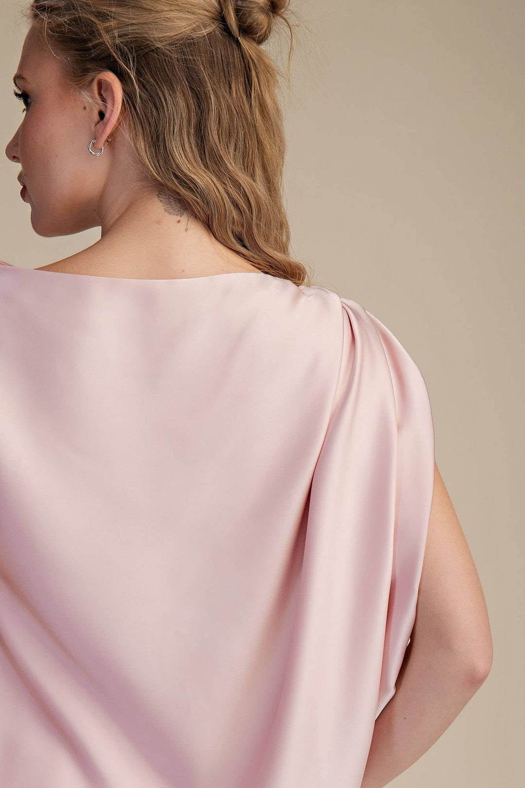 Woman wearing a light pink draped garment against a beige background