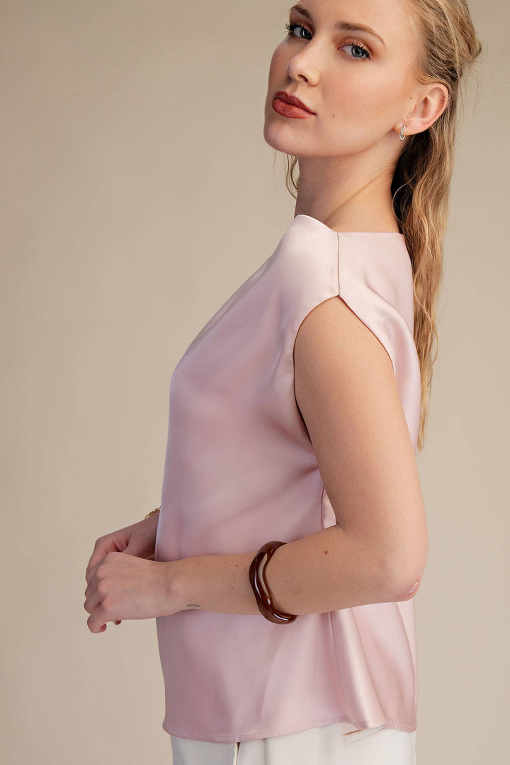 Woman wearing a light pink sleeveless top against a beige background