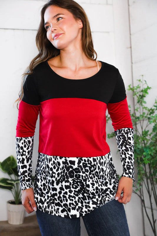 Woman wearing a black and red top with leopard print sleeves indoors.