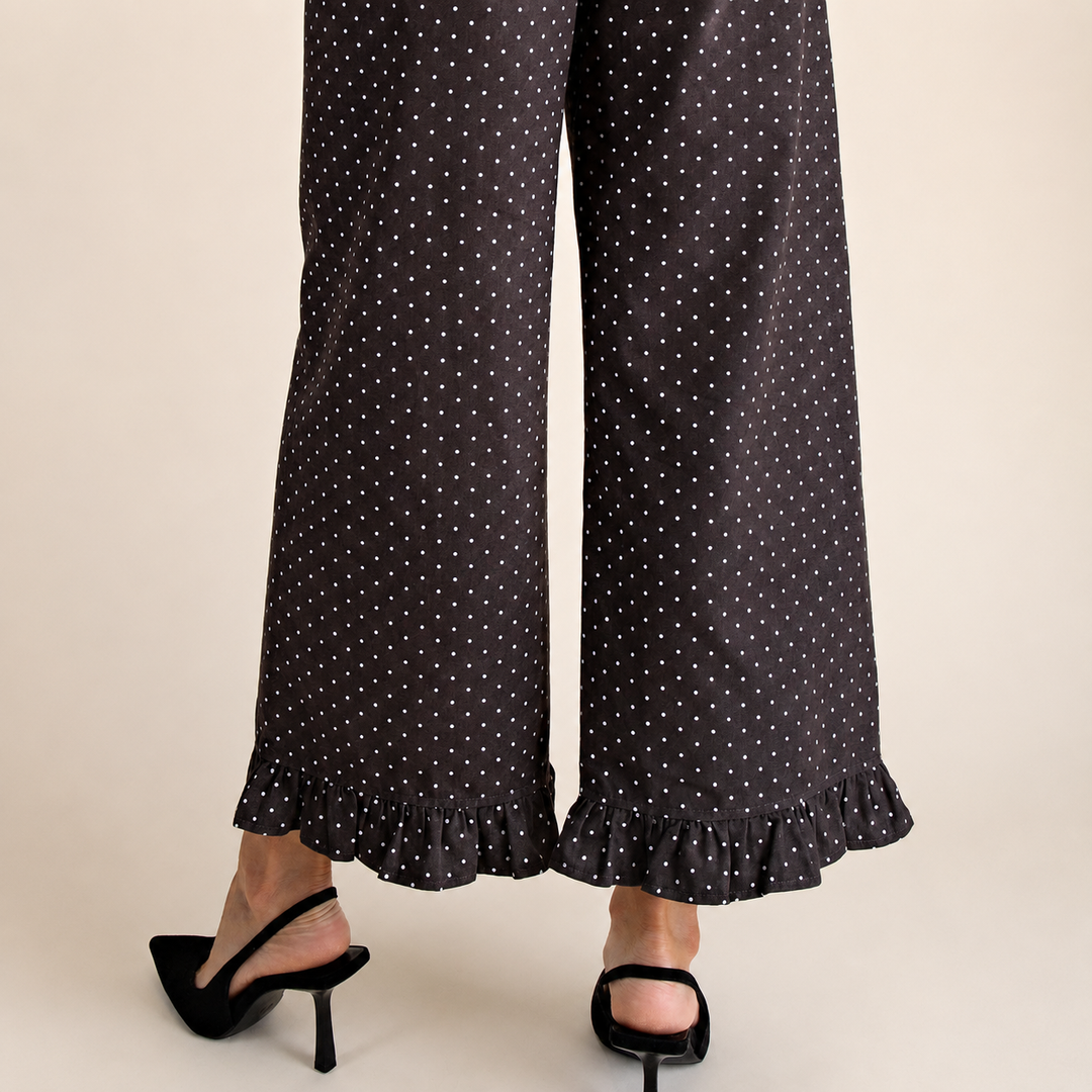 Brown wide-leg pants with a white polka dot pattern and ruffled hems, shown on a model wearing black slingback high heels against a light beige background.