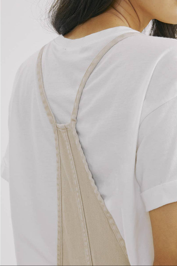 Person wearing a white shirt with beige overalls on a plain background