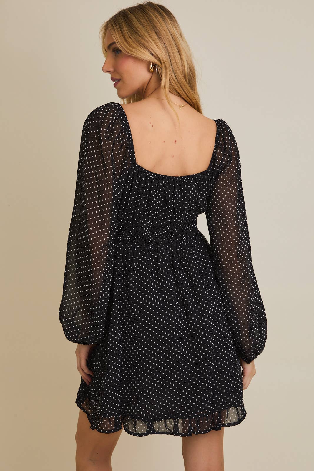 Woman wearing a black polka dot dress with sheer sleeves on a beige background