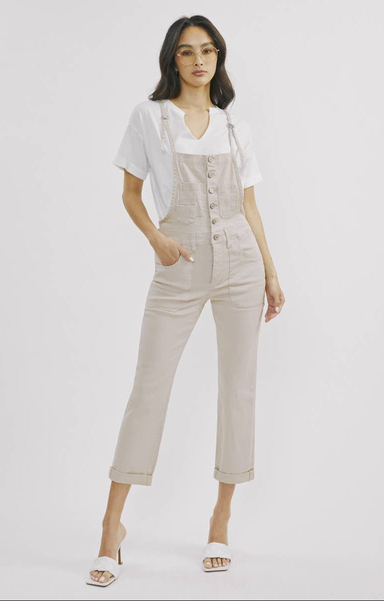 Woman wearing a beige jumpsuit and white shirt on a light gray background