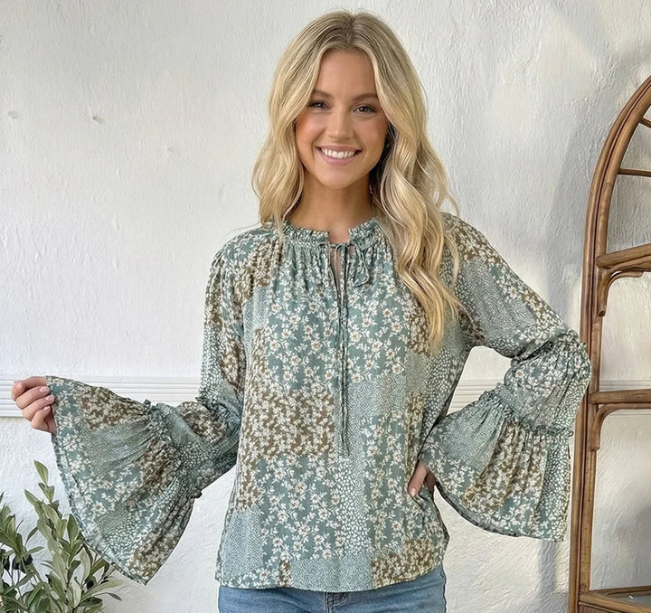 Woman wearing a floral blouse with bell sleeves indoors.