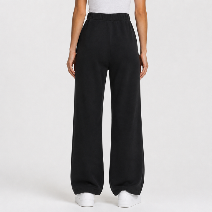 Black wide-leg sweatpants shown on a model from the back, paired with a white top and white sneakers against a light gray studio background.