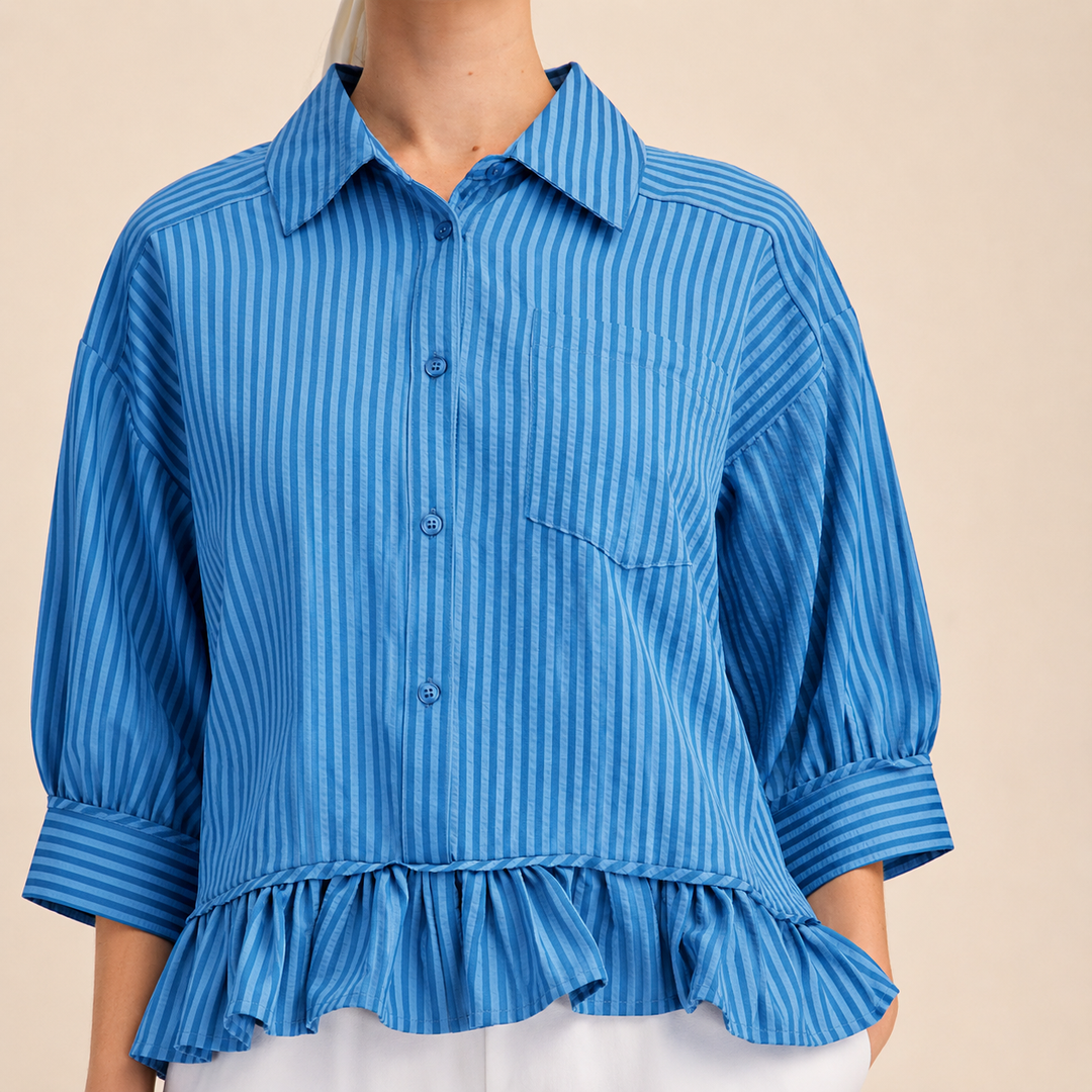 Blue striped shirt with ruffled bottom worn by a person on a beige background