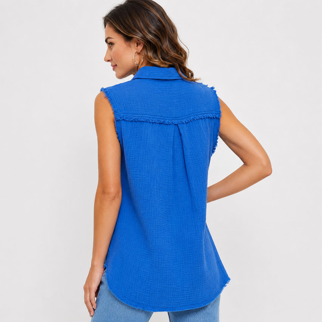 A woman shown from the back wearing a bright blue sleeveless collared shirt with frayed trim details, paired with light blue jeans, against a plain light gray background.