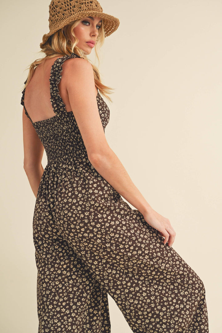 Woman wearing a floral jumpsuit and straw hat on a beige background