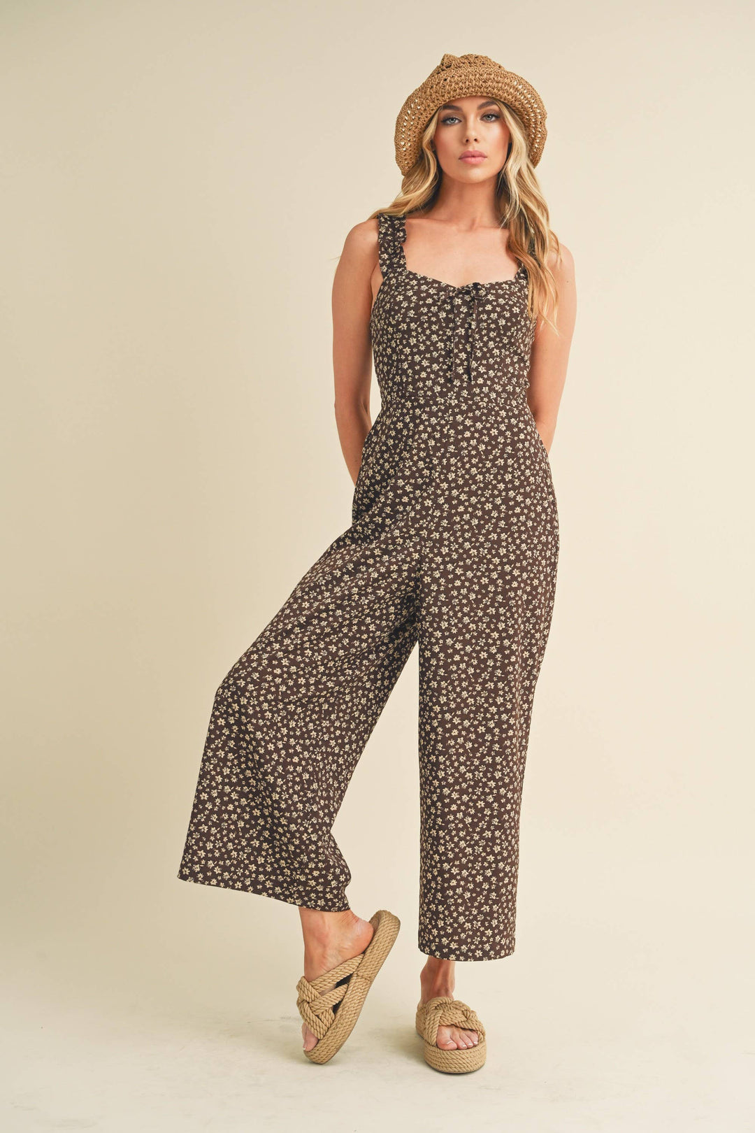 Woman wearing a floral jumpsuit and straw hat on a beige background