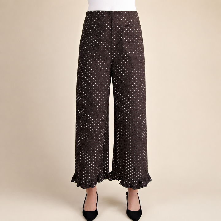 Brown wide-leg pants with a small white polka dot pattern and a ruffled hem, shown on a model wearing black pointed-toe heels against a solid beige background.