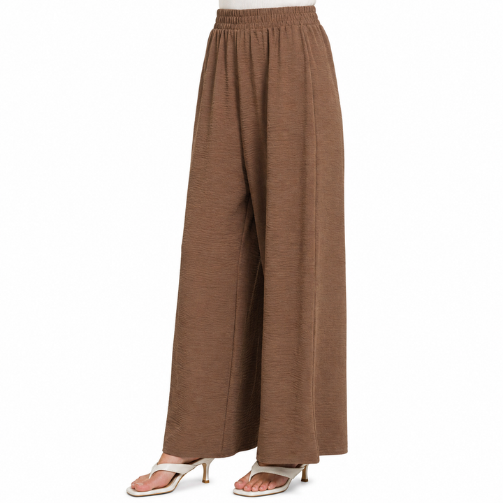 A pair of wide-leg, high-waisted pants in a textured brown fabric, shown on a model from the waist down wearing white heeled sandals against a plain white background.