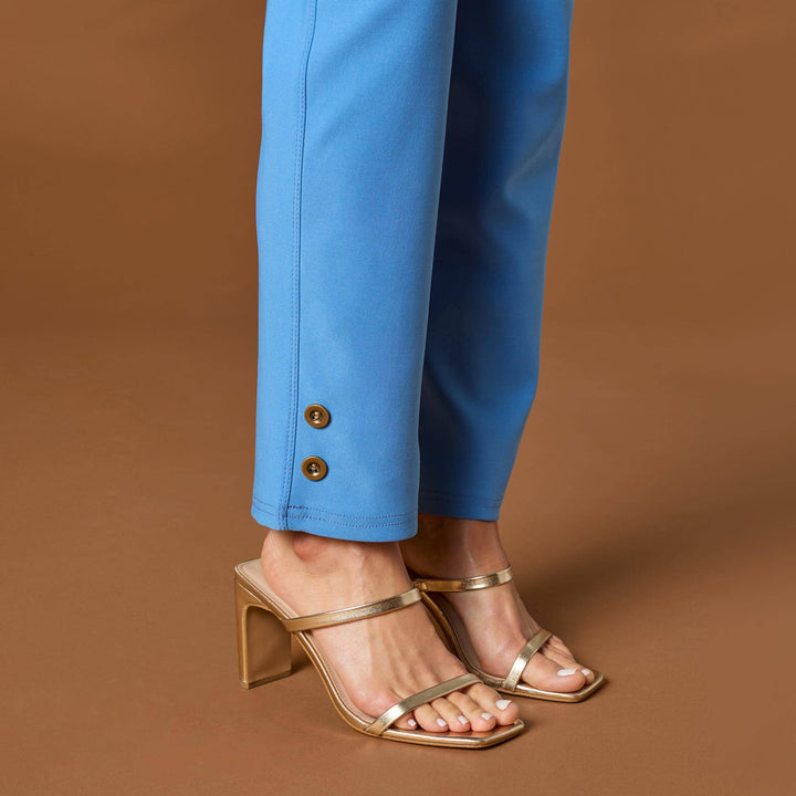 Blue pants with gold buttons and gold high-heeled sandals on a brown background