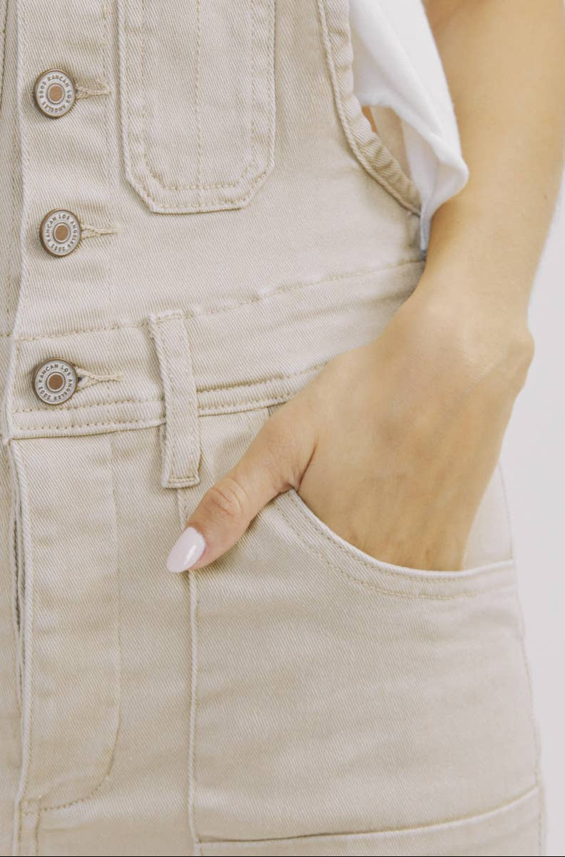 Close-up of beige denim overalls with a hand in the pocket on a white background