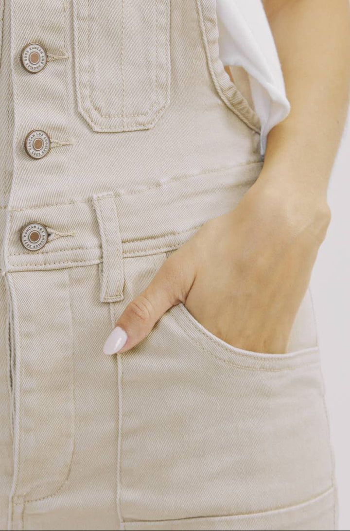 Close-up of beige denim overalls with a hand in the pocket on a white background