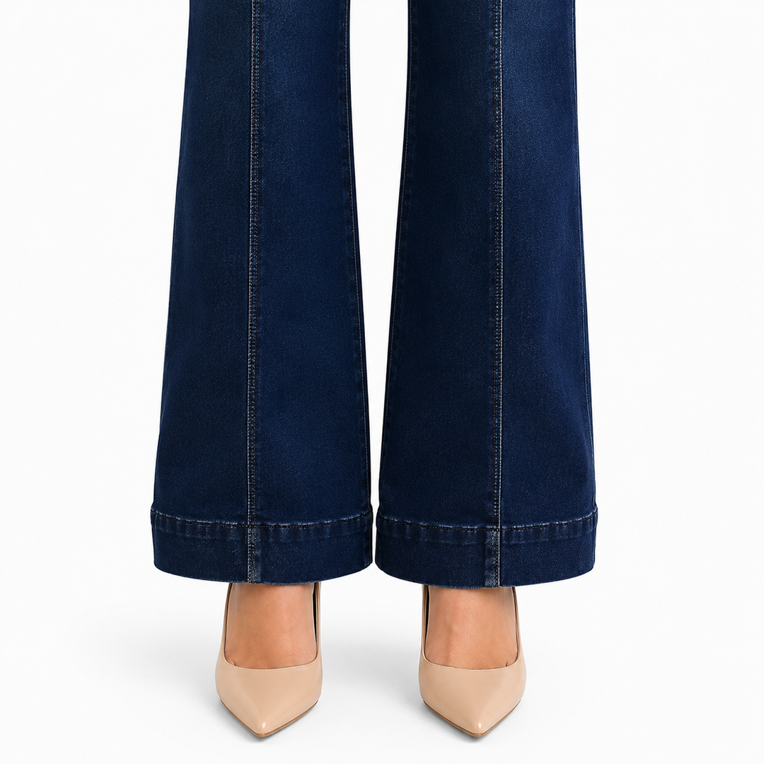 Dark blue flared jeans shown from the knees down, paired with beige pointed-toe heels on a plain white background.