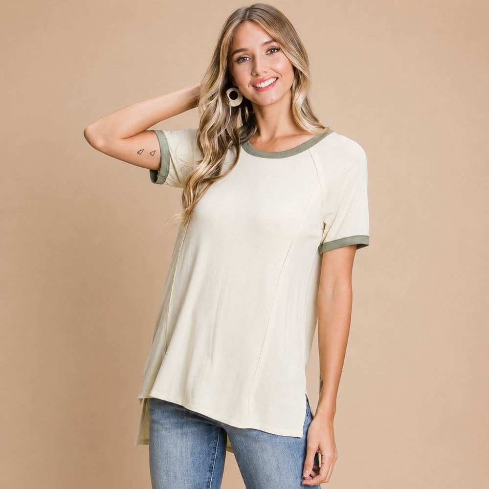 Woman wearing a beige and green short-sleeve top with blue jeans on a beige background