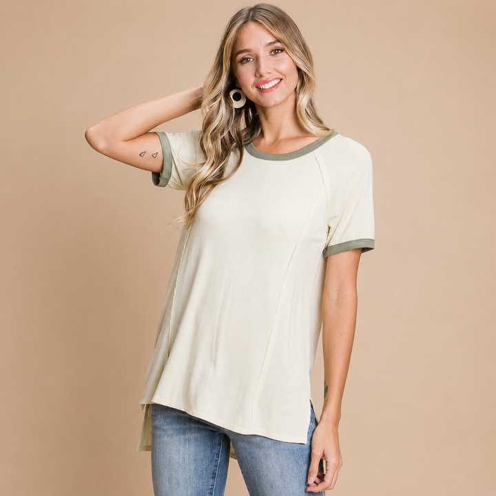 Woman wearing a beige and green short-sleeve top with blue jeans on a beige background