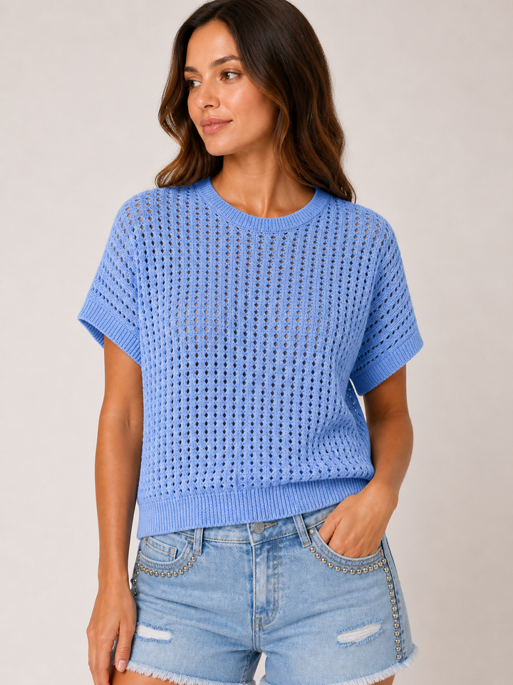 Woman wearing a blue knitted top and denim shorts on a plain background