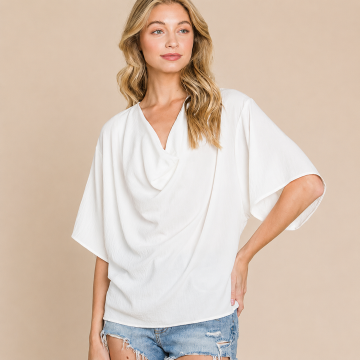Woman wearing a white draped top and denim shorts on a beige background