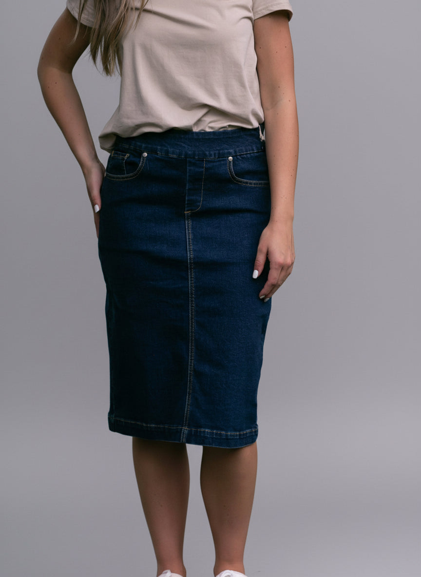Person wearing a beige shirt and blue denim skirt standing outdoors with a blurred green background