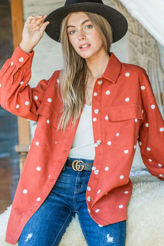 Woman wearing a red polka dot shirt, black hat, and blue jeans indoors.