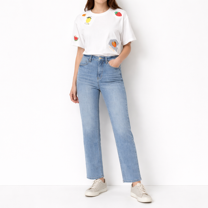 Person wearing a white t-shirt with colorful fruit designs and light blue jeans on a white background