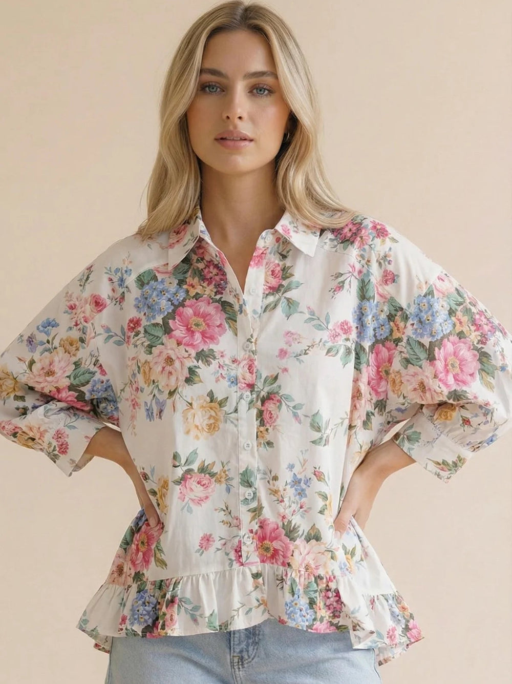 Woman wearing a floral blouse and denim shorts against a beige background