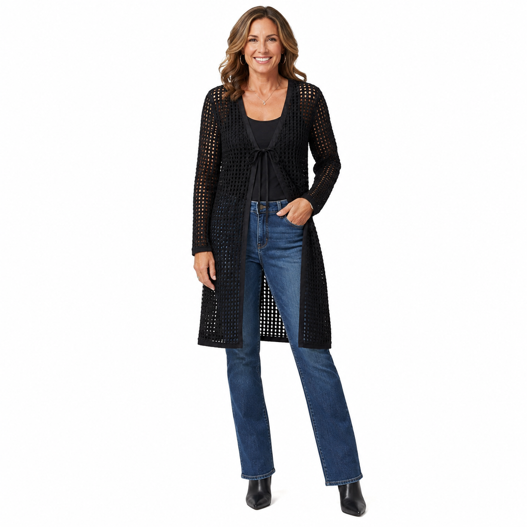 A woman modeling a black open-front knit cardigan with a textured openwork pattern, worn over a black top and blue jeans, against a plain white background.