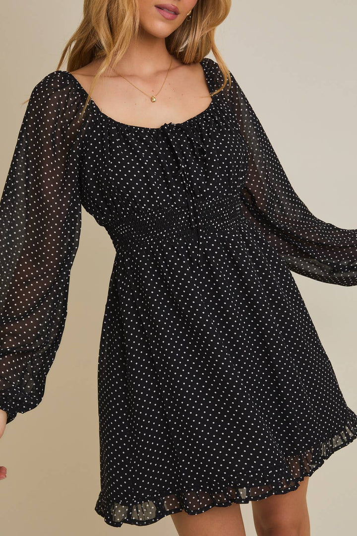 Black polka dot dress with sheer long sleeves on a neutral background