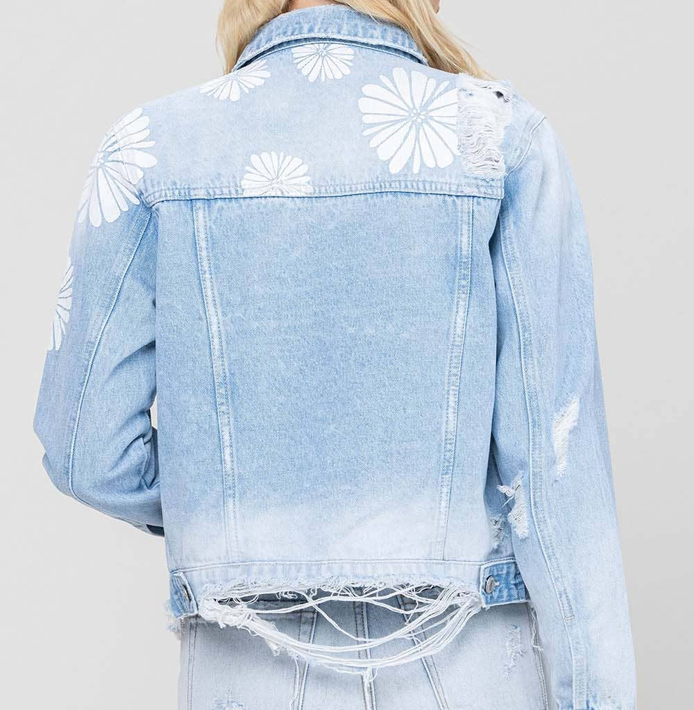 Light blue denim jacket with floral patterns and distressed denim shorts on a plain background