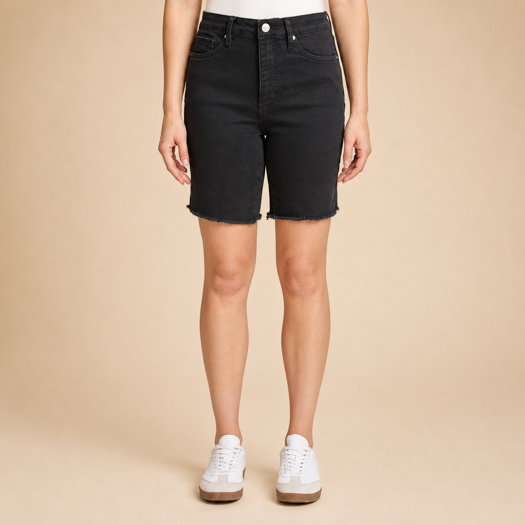Person wearing black denim shorts on a beige background