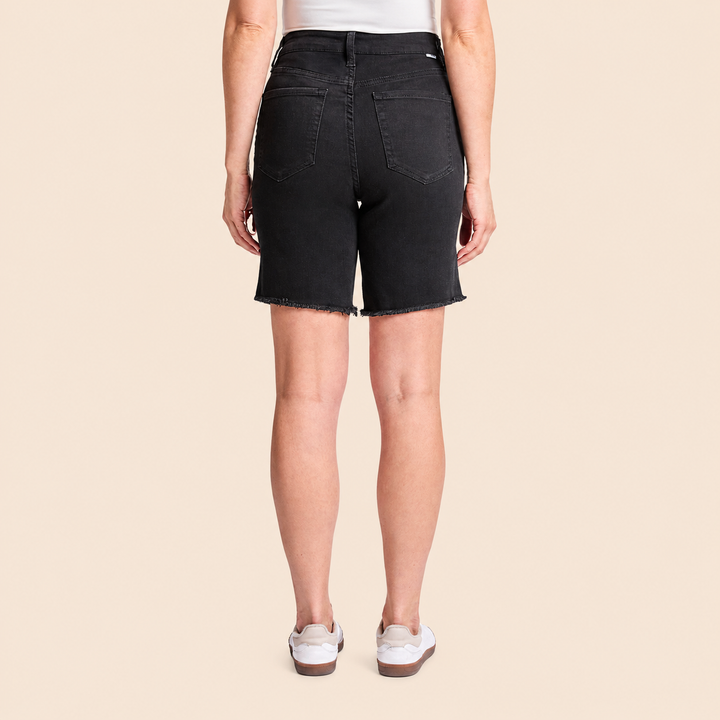 Person wearing black denim shorts on a beige background