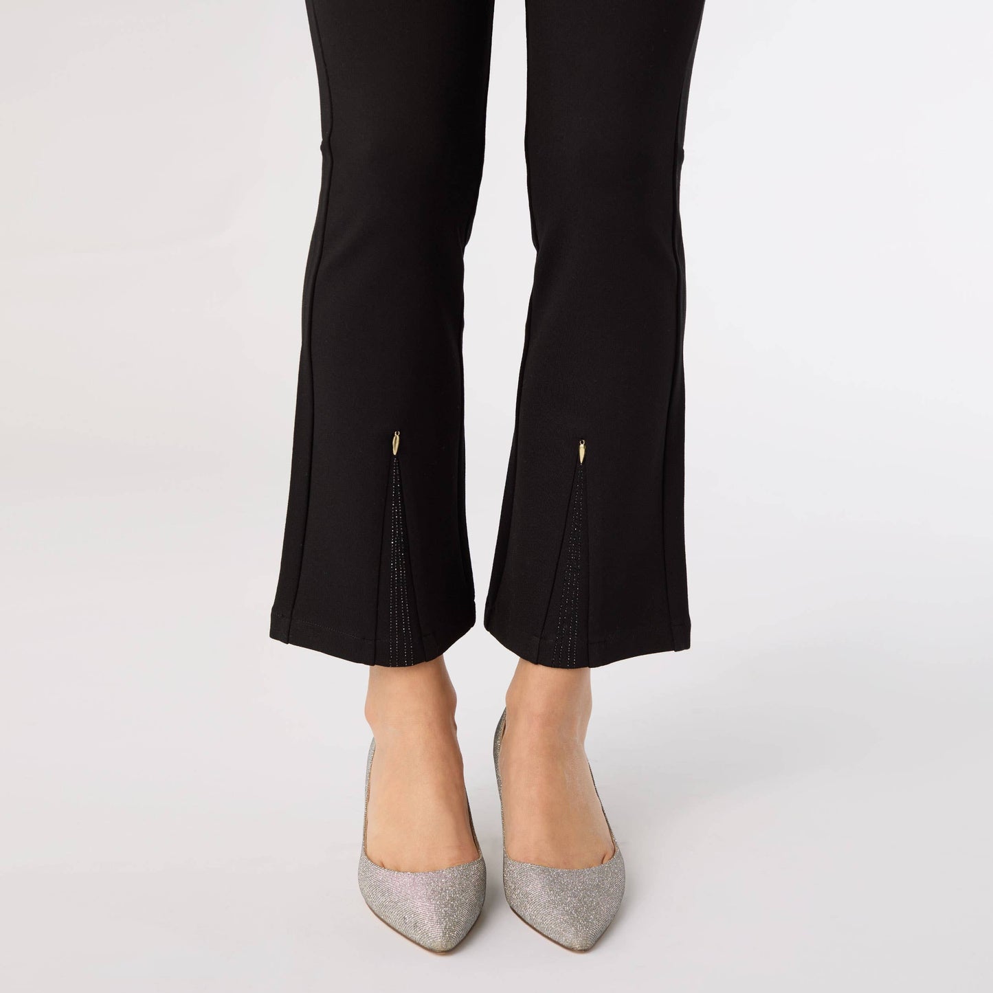 Black pants with cut-out details worn by a person on a white background