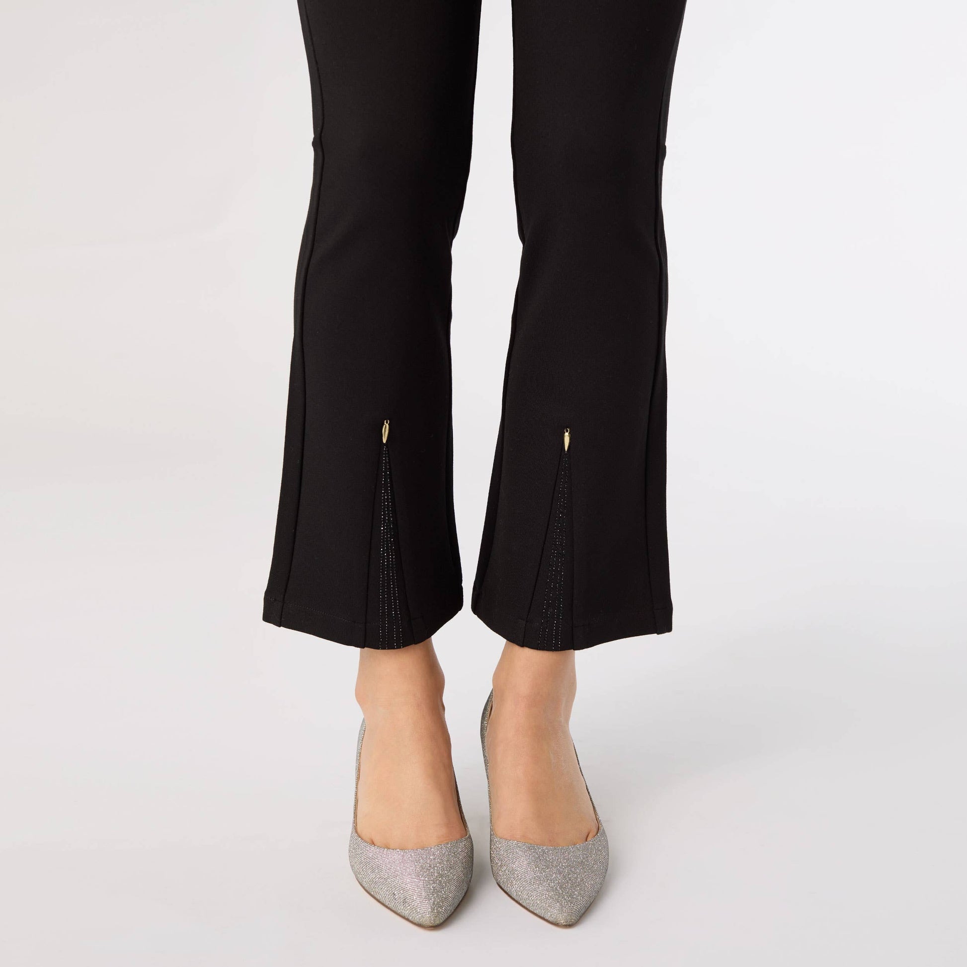 Black pants with cut-out details worn by a person on a white background