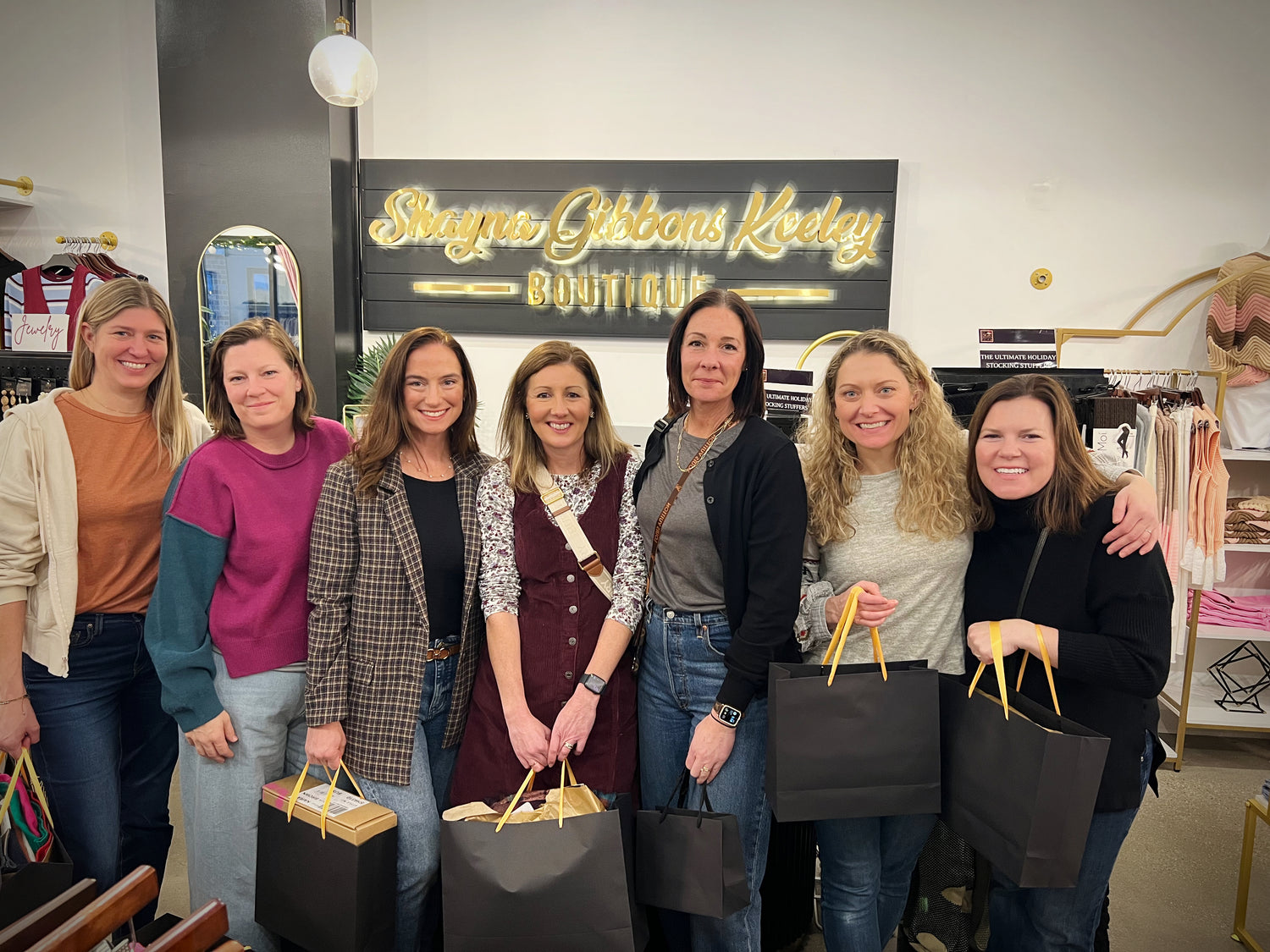 Group of women posing with shopping bags in a store.