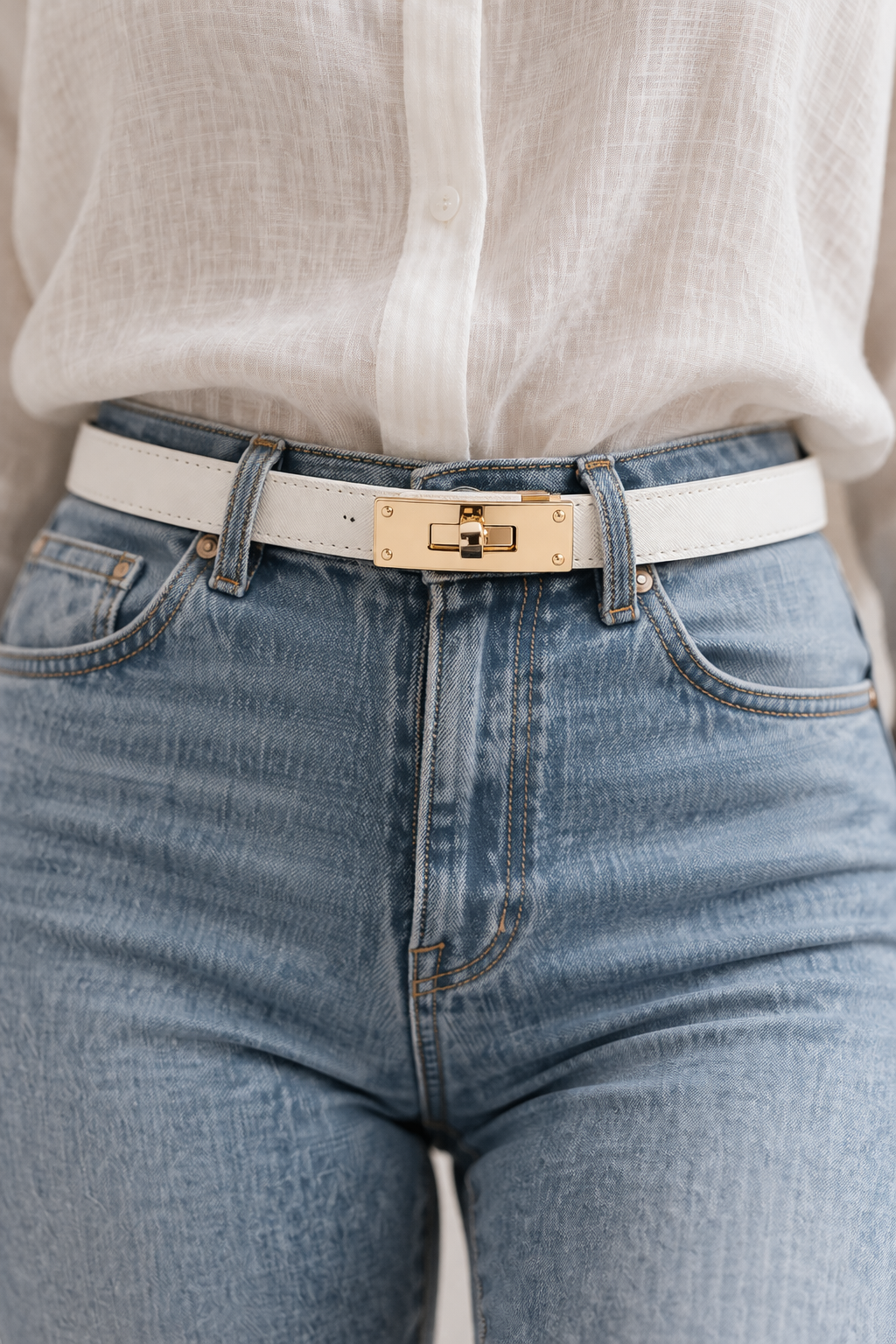 Close-up of blue jeans with a gold belt buckle and white shirt.