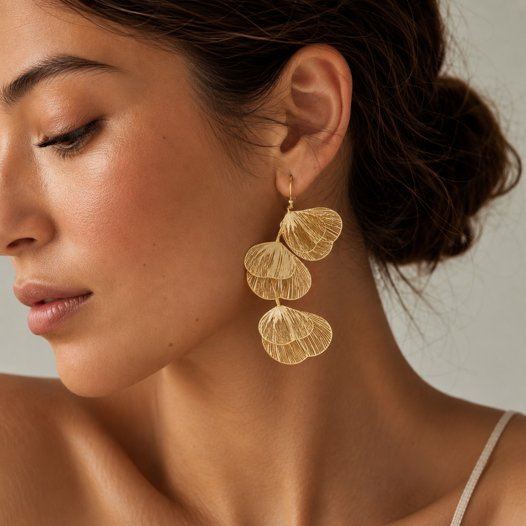 Close-up of a woman wearing gold leaf-shaped earrings against a neutral background