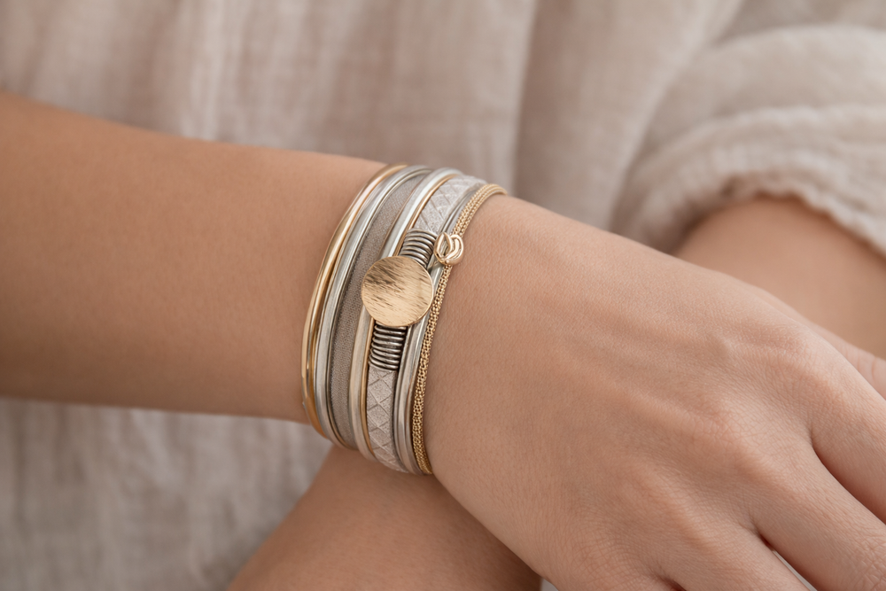 Close-up of a wrist wearing multiple gold and silver bracelets on a neutral background