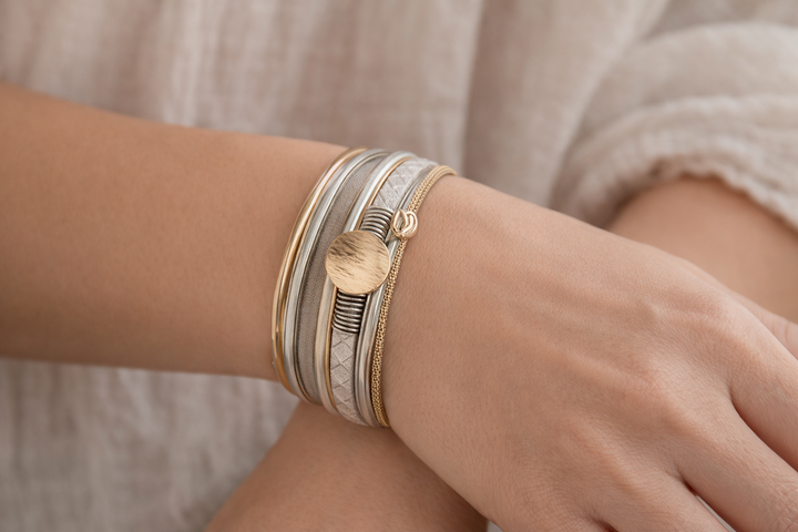 Close-up of a wrist wearing multiple gold and silver bracelets on a neutral background