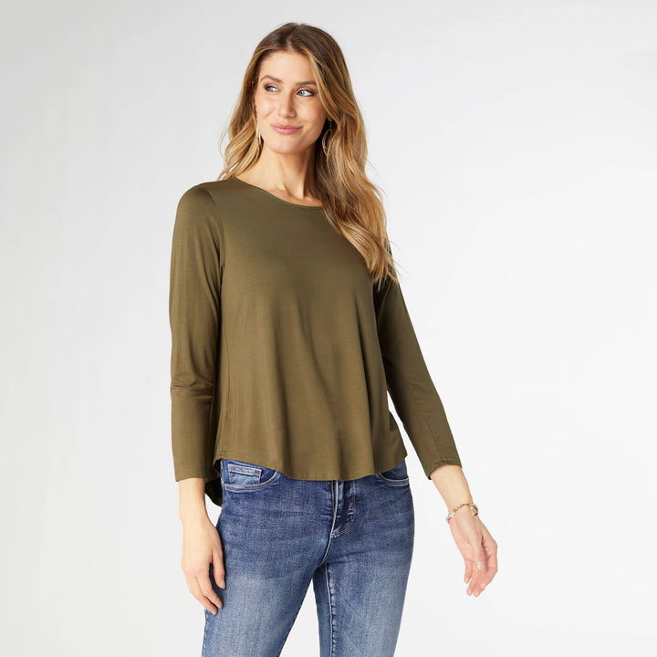 Woman wearing an olive green long-sleeve top and blue jeans on a white background