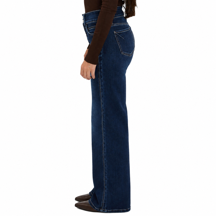 A side profile view of a model wearing dark blue high-waisted flare jeans, a brown long-sleeve top, and brown shoes against a plain white background.
