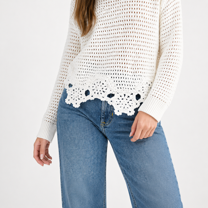Person wearing a white crochet sweater and blue jeans on a white background