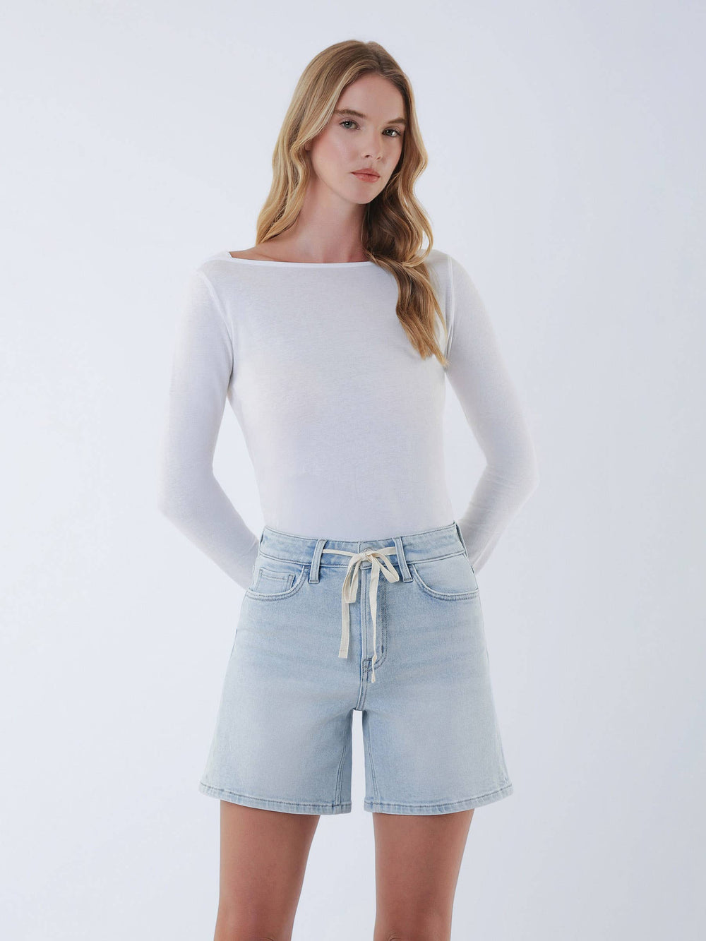 Woman wearing a white long-sleeve top and light blue denim shorts on a white background