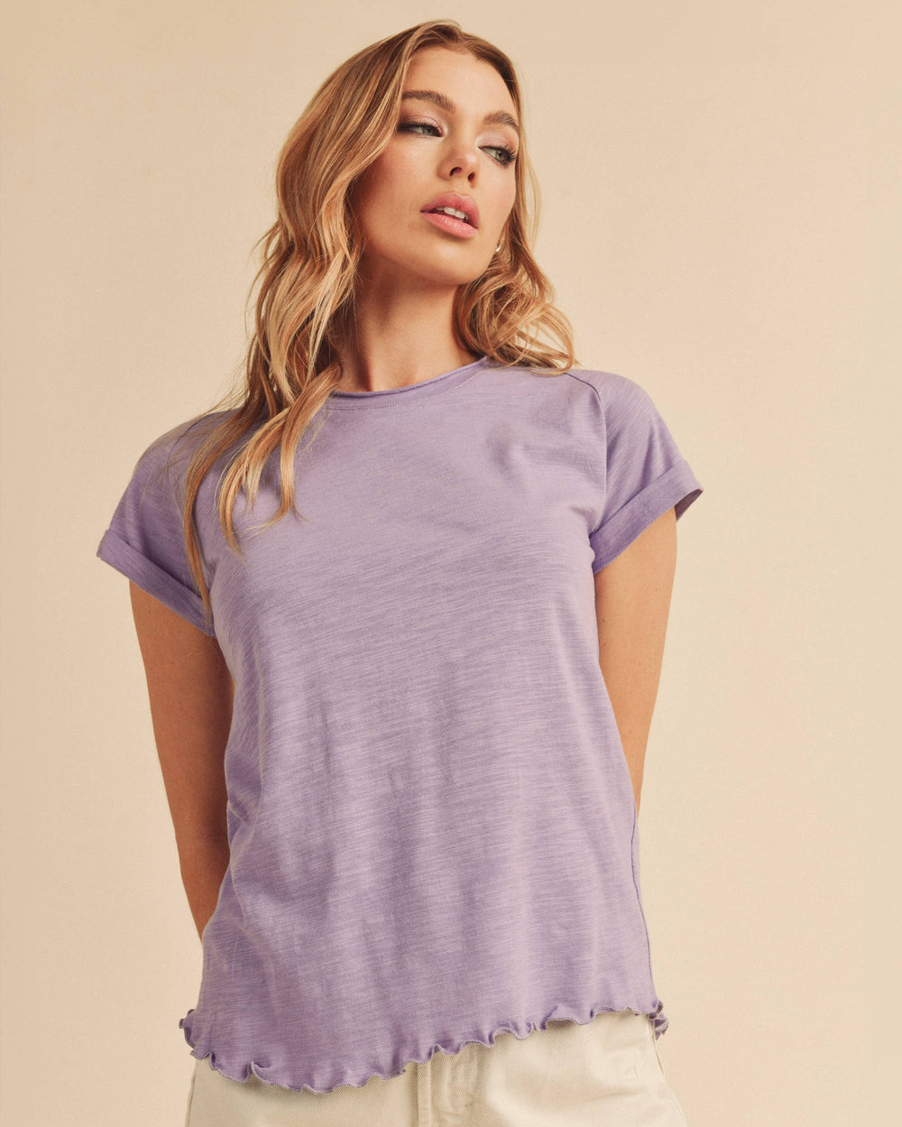 Woman wearing a purple t-shirt and beige shorts on a beige background