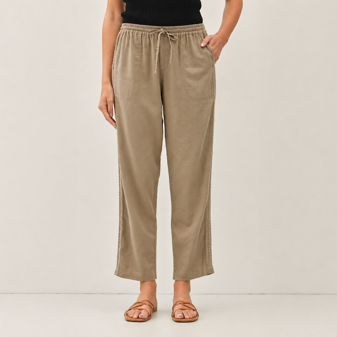 A model is wearing beige wide-leg cropped pants with a drawstring waist, paired with a black top and brown strappy sandals, against a plain light gray studio background.
