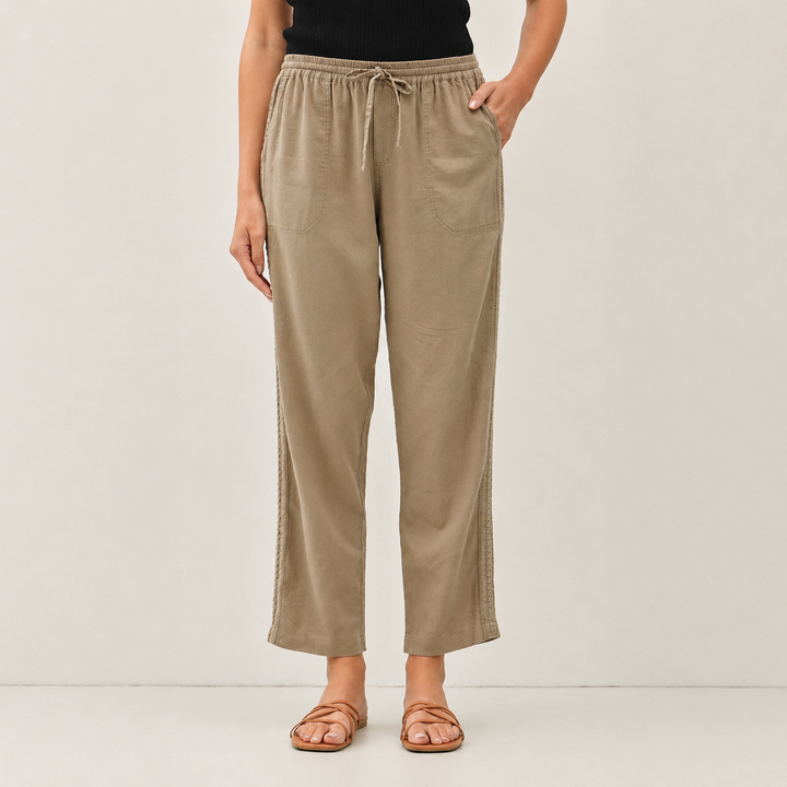 A model is wearing beige wide-leg cropped pants with a drawstring waist, paired with a black top and brown strappy sandals, against a plain light gray studio background.